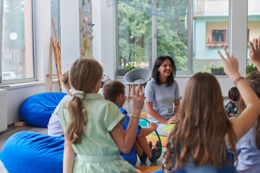 A happy female teacher sitting and playing hand games with a group of little schoolchildren.