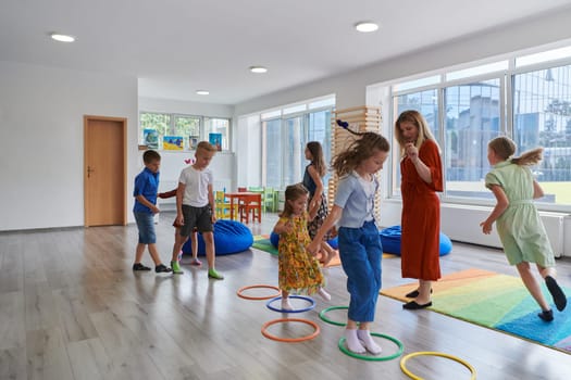 Small nursery school children with female teacher on floor indoors in classroom, doing exercise. Jumping over hula hoop circles track on the floor