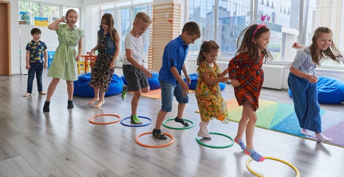 Small nursery school children with female teacher on floor indoors in classroom, doing exercise. Jumping over hula hoop circles track on the floor