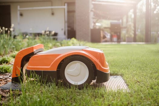An orange robotic lawn mower stands on the base and is charged from electricity in the courtyard.