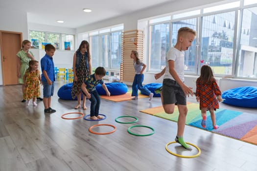 Small nursery school children with female teacher on floor indoors in classroom, doing exercise. Jumping over hula hoop circles track on the floor