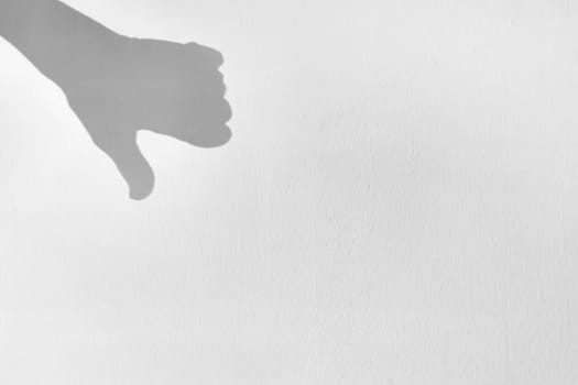 Shadow silhouette of hand with thumb down, on gray background, symbol of disapproval, copy space, noise