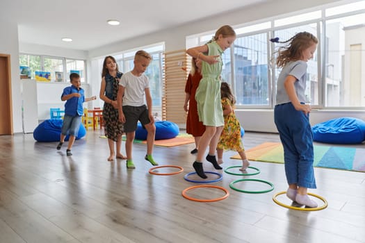 Small nursery school children with female teacher on floor indoors in classroom, doing exercise. Jumping over hula hoop circles track on the floor