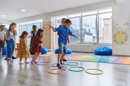 Small nursery school children with female teacher on floor indoors in classroom, doing exercise. Jumping over hula hoop circles track on the floor