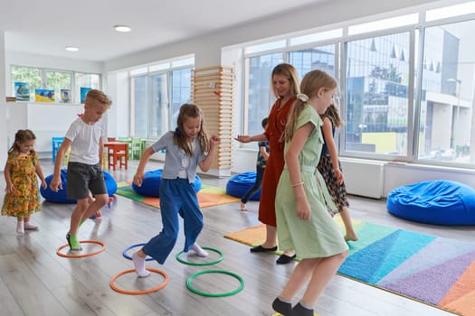 Small nursery school children with female teacher on floor indoors in classroom, doing exercise. Jumping over hula hoop circles track on the floor