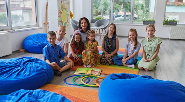 A happy female teacher sitting and playing hand games with a group of little schoolchildren.