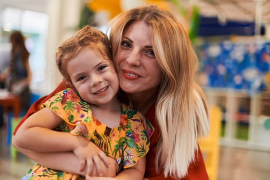 A cute little girl kissing and hugs her mother in preschool. High quality photo