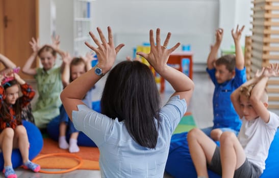 A happy female teacher sitting and playing hand games with a group of little schoolchildren.