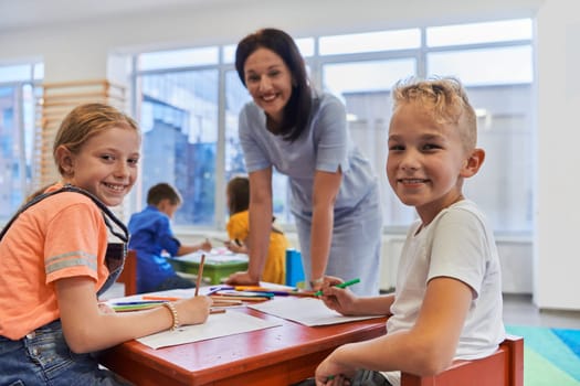 Creative kids during an art class in a daycare center or elementary school classroom drawing with female teacher