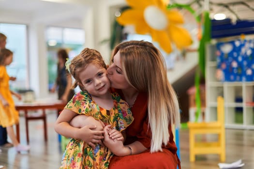 A cute little girl kissing and hugs her mother in preschool. High quality photo