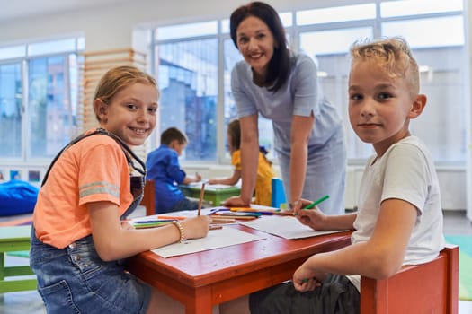 Creative kids during an art class in a daycare center or elementary school classroom drawing with female teacher