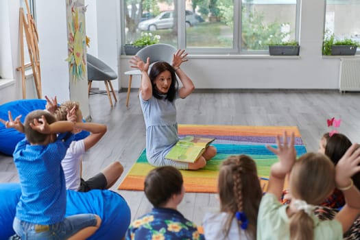 A happy female teacher sitting and playing hand games with a group of little schoolchildren.