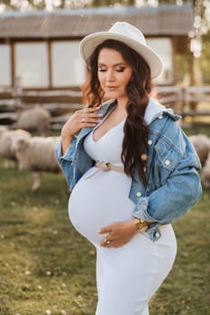 Stylish pregnant woman in a white hat in the countryside.