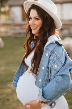 Stylish pregnant woman in a white hat in the countryside.