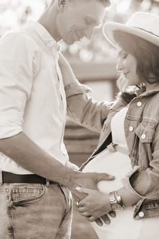 Happy man hugs his pregnant woman's belly at sunset.