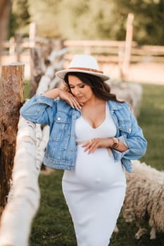 Stylish pregnant woman in a white hat in the countryside.