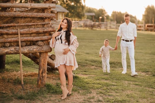 A stylish family in the countryside at sunset. A pregnant woman with her husband and son in nature.