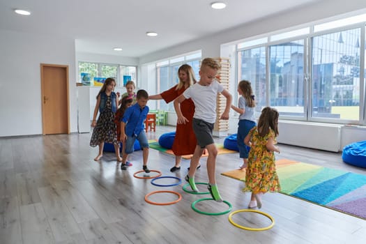 Small nursery school children with female teacher on floor indoors in classroom, doing exercise. Jumping over hula hoop circles track on the floor