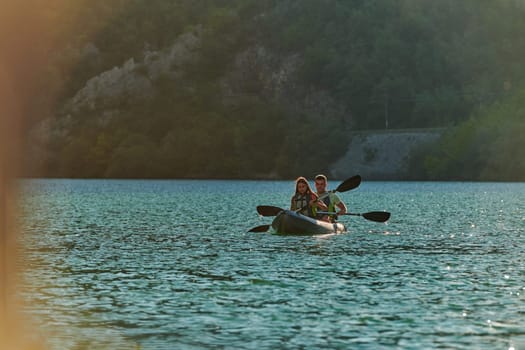 A young couple enjoying an idyllic kayak ride in the middle of a beautiful river surrounded by forest greenery in sunset time.