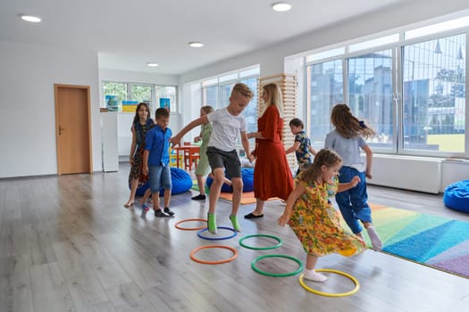 Small nursery school children with female teacher on floor indoors in classroom, doing exercise. Jumping over hula hoop circles track on the floor