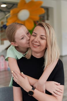 A cute little girl kisses and hugs her mother in preschool. High quality photo