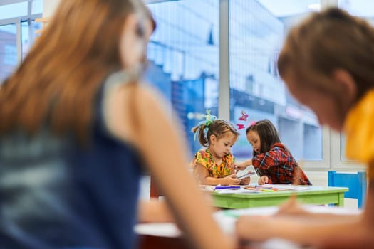 Creative kids during an art class in a daycare center or elementary school classroom drawing with female teacher