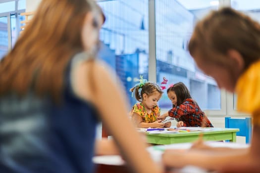 Creative kids during an art class in a daycare center or elementary school classroom drawing with female teacher