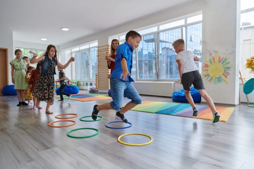 Small nursery school children with female teacher on floor indoors in classroom, doing exercise. Jumping over hula hoop circles track on the floor