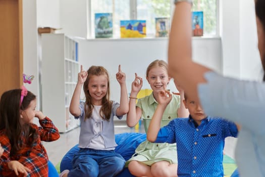 A happy female teacher sitting and playing hand games with a group of little schoolchildren.