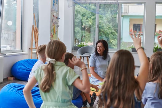 A happy female teacher sitting and playing hand games with a group of little schoolchildren.