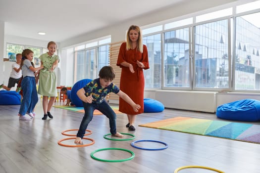 Small nursery school children with female teacher on floor indoors in classroom, doing exercise. Jumping over hula hoop circles track on the floor