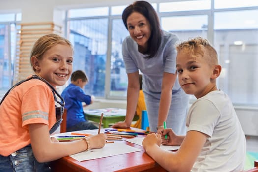 Creative kids during an art class in a daycare center or elementary school classroom drawing with female teacher