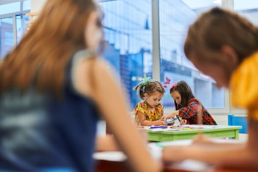 Creative kids during an art class in a daycare center or elementary school classroom drawing with female teacher