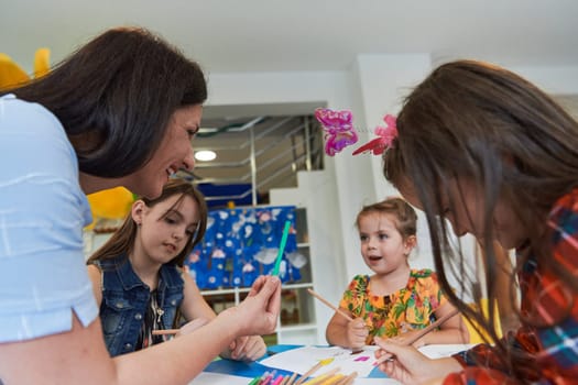 Creative kids during an art class in a daycare center or elementary school classroom drawing with female teacher