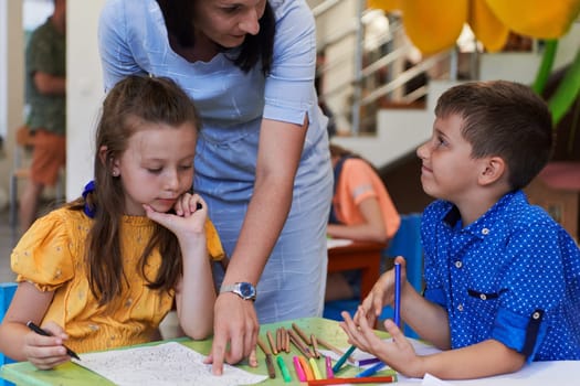 Creative kids during an art class in a daycare center or elementary school classroom drawing with female teacher