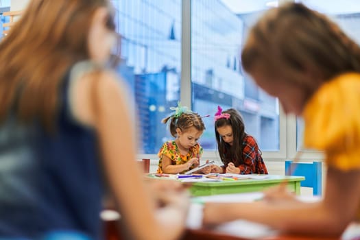 Creative kids during an art class in a daycare center or elementary school classroom drawing with female teacher