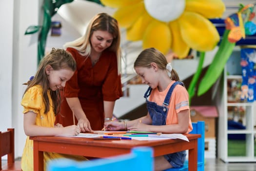 Creative kids during an art class in a daycare center or elementary school classroom drawing with female teacher