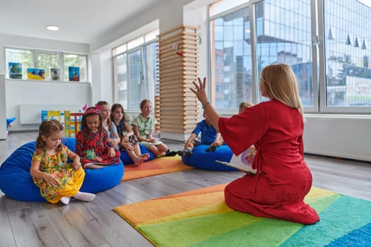 A happy female teacher sitting and playing hand games with a group of little schoolchildren.