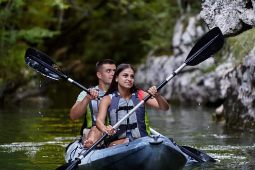 A young couple enjoying an idyllic kayak ride in the middle of a beautiful river surrounded by forest greenery.