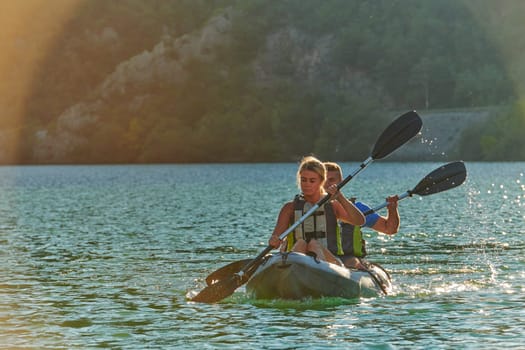 A young couple enjoying an idyllic kayak ride in the middle of a beautiful river surrounded by forest greenery in sunset time.