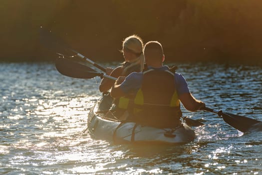 A young couple enjoying an idyllic kayak ride in the middle of a beautiful river surrounded by forest greenery in sunset time.