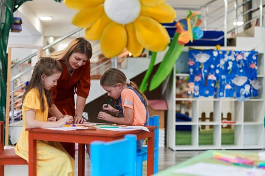 Creative kids during an art class in a daycare center or elementary school classroom drawing with female teacher