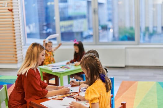 Creative kids during an art class in a daycare center or elementary school classroom drawing with female teacher