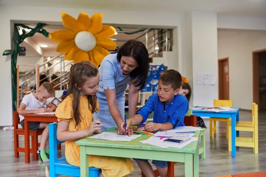 Creative kids during an art class in a daycare center or elementary school classroom drawing with female teacher