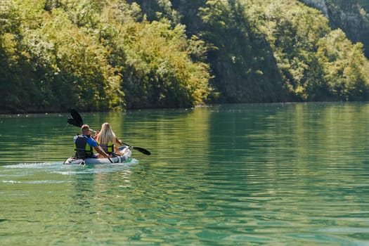 A young couple enjoying an idyllic kayak ride in the middle of a beautiful river surrounded by forest greenery.