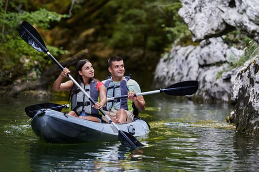 A young couple enjoying an idyllic kayak ride in the middle of a beautiful river surrounded by forest greenery.