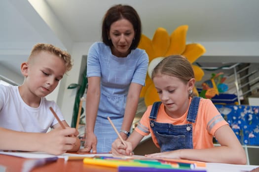 Creative kids during an art class in a daycare center or elementary school classroom drawing with female teacher