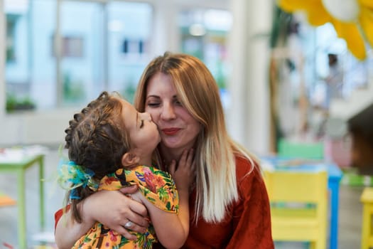 A cute little girl kissing and hugs her mother in preschool. High quality photo