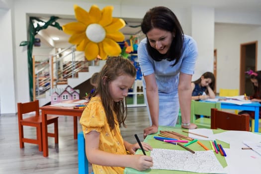 Creative kids during an art class in a daycare center or elementary school classroom drawing with female teacher