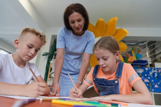 Creative kids during an art class in a daycare center or elementary school classroom drawing with female teacher